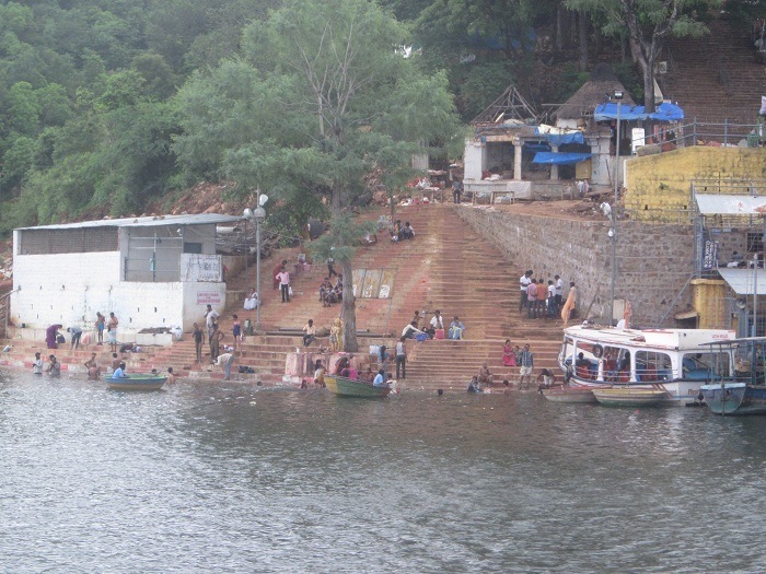 Devotees at the Pathala Ganga ghat in Srisailam taking a holy dip in the Krishna River, with steps leading to the water, surrounded by greenery and boats near Mallikarjuna Swamy Jyotirlinga