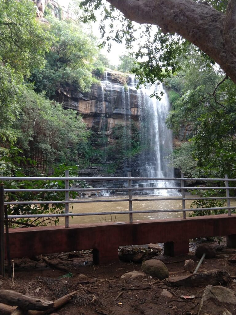 Mallela Theertham Waterfalls cascading down rocky cliffs into a forest pool, framed by lush green trees and a viewing platform, a scenic trekking and nature spot in the Nallamala forest