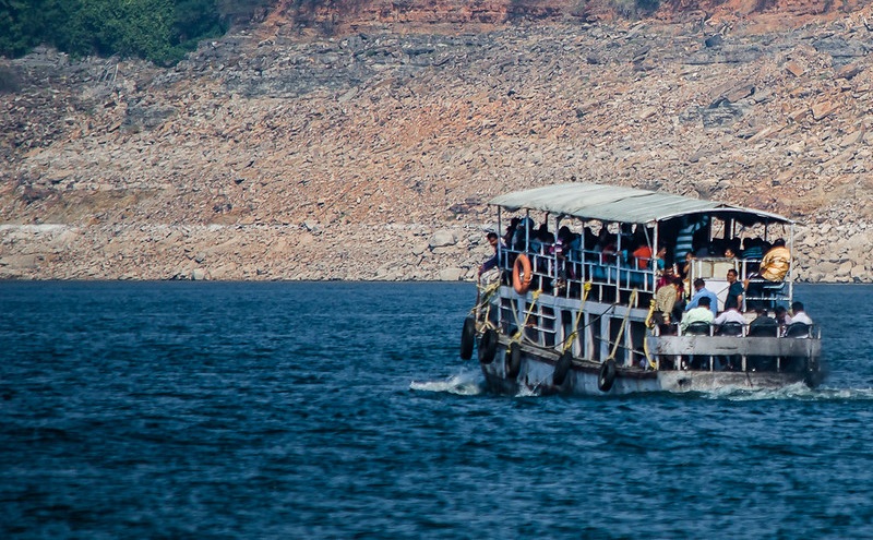 Tourist boat ferrying visitors across the Nagarjunasagar reservoir, with rocky hills and dense greenery in the backdrop