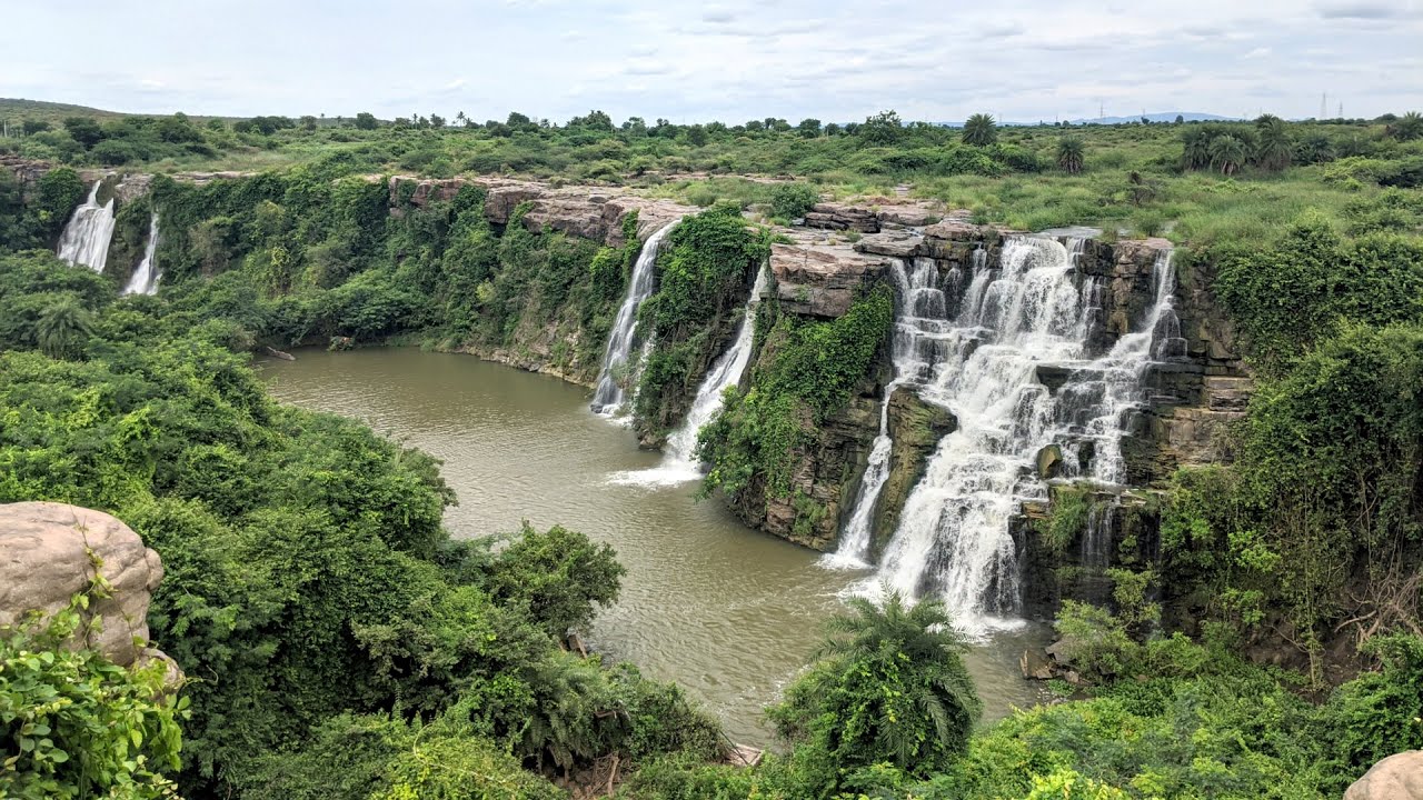 Ethipothala Waterfalls cascading over rocky cliffs into a serene river surrounded by lush green vegetation, a popular tourist attraction and scenic nature spot near Nagarjunasagar